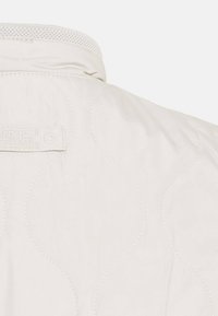 Helle, gesteppte Jacke mit einem strukturierten Muster, einem Stehkragen und einem Etikett mit der Aufschrift "ormel Active" auf der Rückseite.