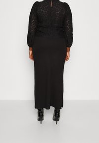 Sort blonderet top med pufærmer, parret med en lang sort nederdel. Outfittet har en tætsiddende silhuet og en nøglehulrygdetalje.