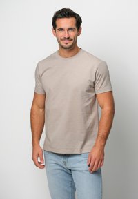 Beige bomull t-shirt med kort ärm och rund halsringning, bärs med ljusblå jeans. Tyget har en mjuk textur med minimala sömmar.