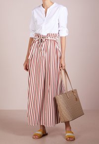 Randiga vida byxor i vitt och rost, knutna i midjan; tillsammans med en vit skjorta med knappar och en beige axelväska. Gula sandaler.