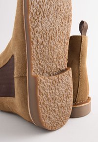 Tan suède enkellaarsjes met elastische zijpanelen en gestructureerde rubberen zolen. Ronde neus en lichte hak; nette stikdetails.