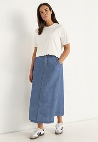 Denim maxikjol i ljusblått, med rak silhuett, framfickor och knappstängning, i kombination med en vit t-shirt och sneakers.