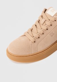 Μπεζ σουέτ αθλητικό παπούτσι με στρογγυλή μύτη, επίπεδα κορδό�νια και λεπτομέρεια με λογότυπο. Υφή καφέ λάστιχο στην σόλα με οριζόντιες ρίγες για καλύτερη πρόσφυση.