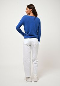 Blå stickad tröja med långa ärmar, matchad med vita raka jeans och ljusa sneakers, sedd bakifrån.