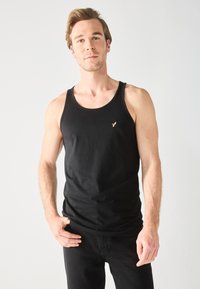Top de tirantes de algodón negro con escote redondo, que cuenta con un pequeño logo bordado en el lado izquierdo. Textura suave y diseño ajustado.