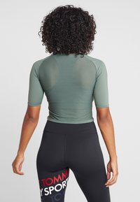 Top deportivo verde de manga corta con tejido de malla texturizada. Combinado con leggings negros de cintura alta que presentan detalles de marca en rojo y blanco.