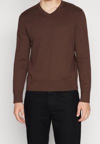 Pull marron à manches longues et col en V en tissu tricoté avec un ourlet ajusté. La texture semble lisse et légèrement extensible.