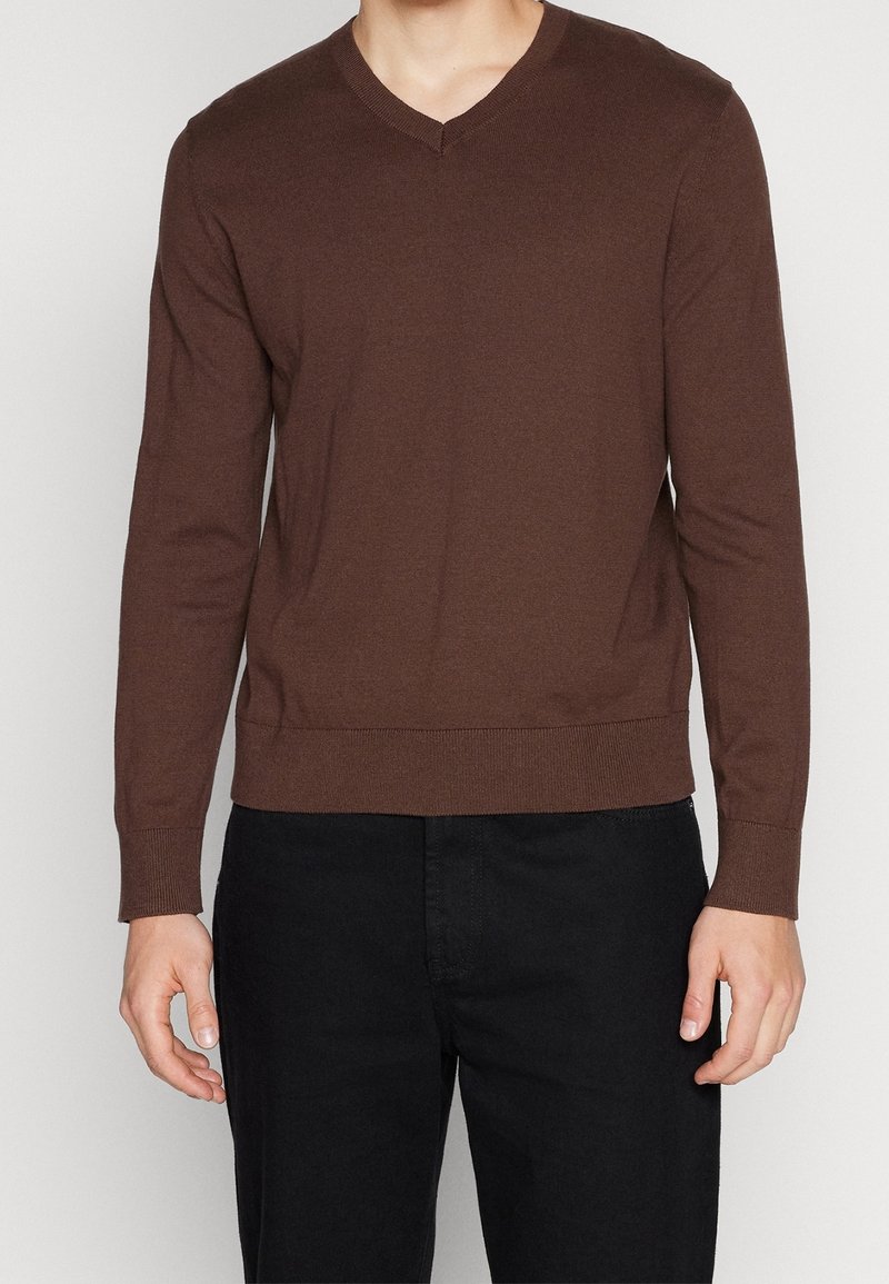 Pull marron à manches longues et col en V en tissu tricoté avec un ourlet ajusté. La texture semble lisse et légèrement extensible.