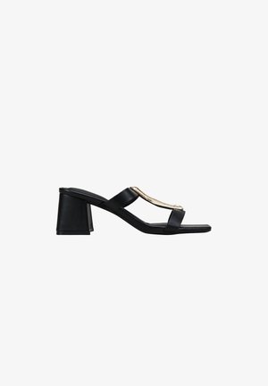 Sandalia mule negra de punta abierta con tacón bloque y dos tiras, una de ellas con un adorno metálico dorado sobre fondo blanco.