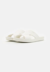 Weiße Riemchensandalen mit einem strukturierten Überkreuz-Design und einer gepolsterten Sohle mit gerilltem Rand. Glattes, flexibles Material überall.