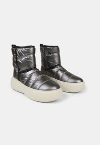 Padded ankle boots in metallic gray with black accents, featuring a zip closure and a thick white sole. Textured surface with quilted design.