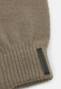 Pletena kapa u prigušenoj maslinastoj boji, izrađena od meke vune. Ima vertikalno rebrasto tkane i crnu kožnu oznaku brenda sa strane.