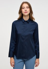 Camicia blu navy a maniche lunghe realizzata in tessuto liscio, con chiusura a bottoni sul davanti, colletto classico e orlo curvo. Nessun motivo o dettaglio visibile.