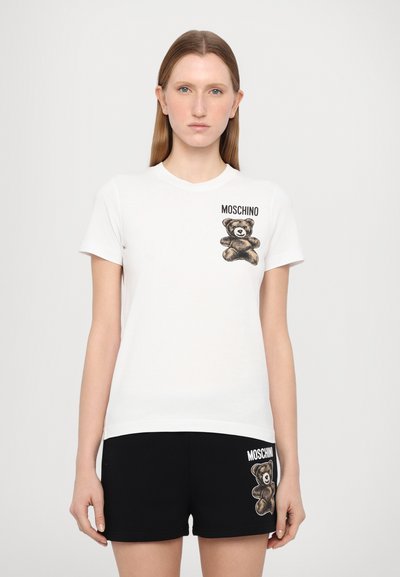 T-shirt en coton blanc avec un motif de teddy bear et le texte "MOSCHINO". Associé à un short noir, les deux affichant un design de ours similaire.