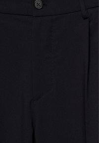 Pantalon noir avec fermeture par bouton et détail de couture visible autour de la braguette.