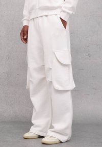 Pantalones cargo blancos hechos de una tela suave con bolsillos laterales, corte holgado y cintura acanalada. Combinados con calzado de color claro.