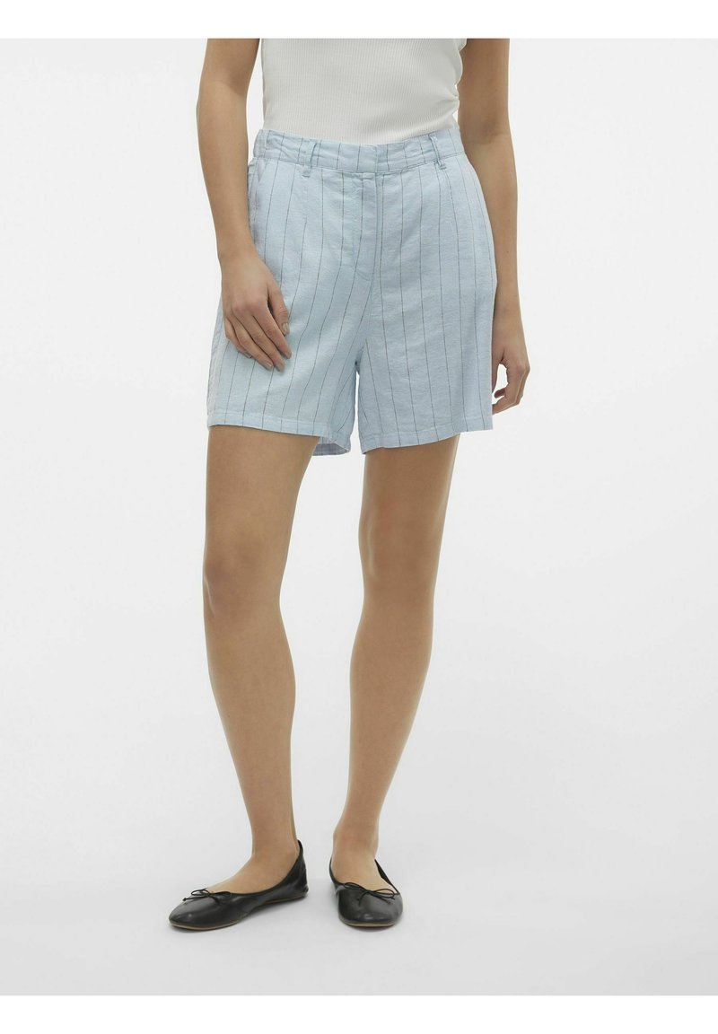 Shorts en lin bleu clair avec des rayures blanches verticales, dotés d'une coupe décontractée et de poches latérales. Portés avec des ballerines noires.