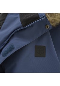 Blå jacka i tyg med slät yta, med en svart logotyp-patch och dragkedjestängning. Krage med pälsfoder och kardborredetaljer.