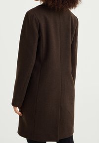 Brun ullkappa med rak silhuett, långa ärmar och skräddarsydd sömn på ryggen. Slät textur med minimala detaljer.