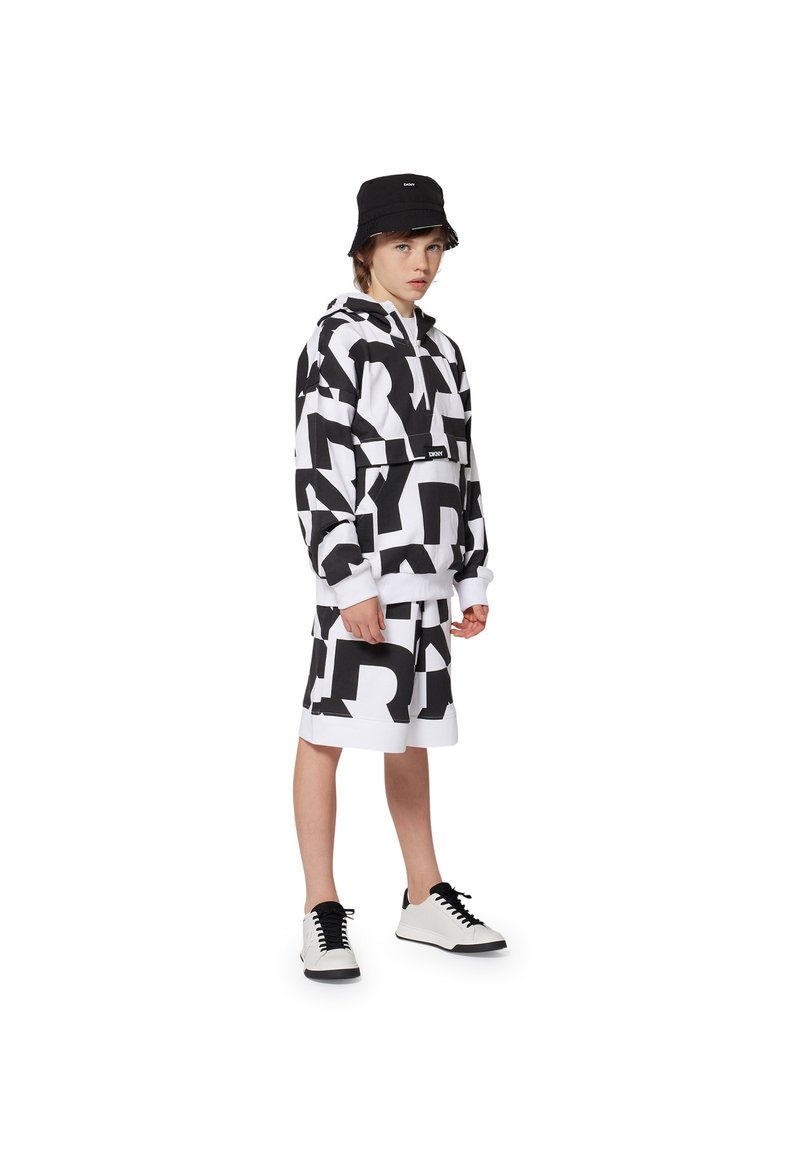 Zwart-wit geblokte sweatshirt en een rok tot de knie, gecombineerd met een zwarte emmerhoed en zwart-witte sneakers, op een neutrale achtergrond.