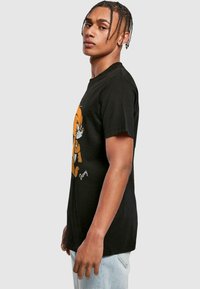 Camiseta de algodón negra con estampado de un personaje de dibujos animados en naranja. Manga corta, cuello redondo, corte relajado y textura suave.
