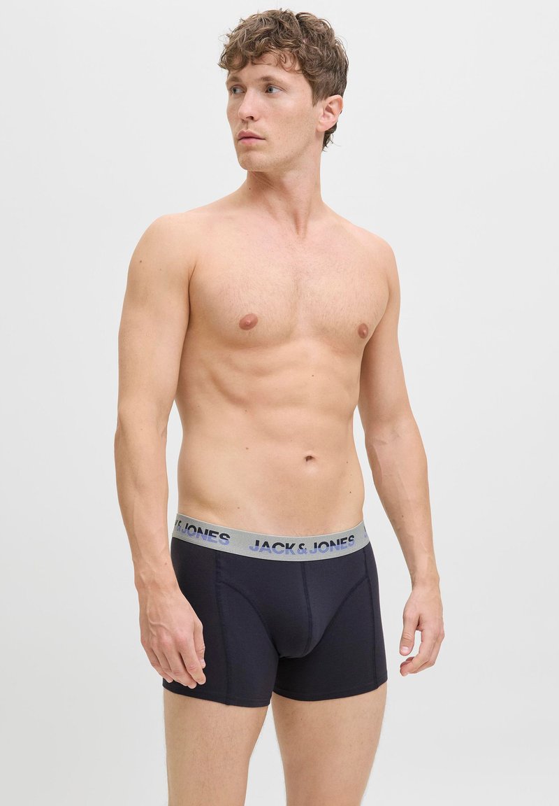 Marinefarbene Boxershorts mit einem grauen Bund, auf dem "JACK & JONES" in Blau gedruckt ist. Der Stoff wirkt glatt und elastisch. Das Modell ist oberkörperfrei.