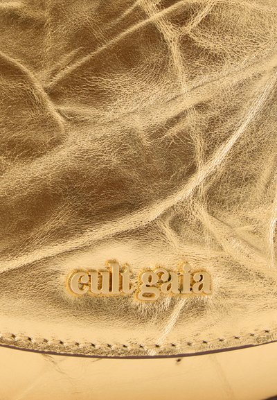 Zlatá kožená plocha s mačkanou texturou a viditelným švem. Obsahuje embosované jméno značky "cult gaia" v tučném písmu.