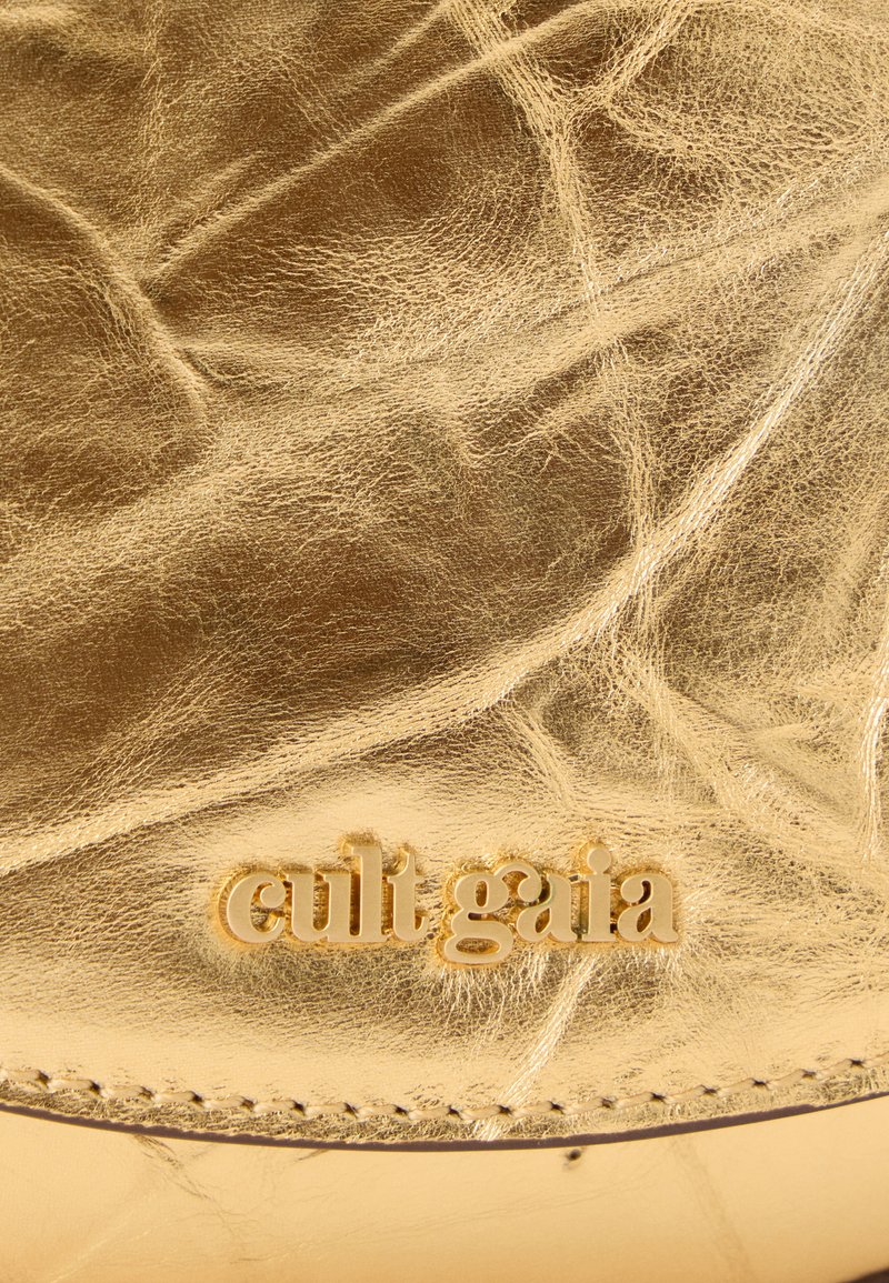 Superficie in pelle dorata con una texture raggrinzita e cuciture visibili. Presenta il nome del marchio in rilievo "cult gaia" in un carattere audace.