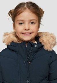 Marineblauwe pufferjack met een met bont gevoerde capuchon, voorzien van een ritssluiting en drukknoopjes, gebroken textuur en bruine bontaccenten op de capuchon.
