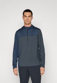 Hooded long-sleeve top in dark blue, featuring a contrasting panel and half zipper at the neck. Soft, lightweight fabric with a relaxed fit.