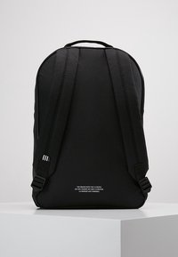 Black backpack with a sleek design, featuring padded straps, textured fabric, and a minimalistic logo in white on the lower front.