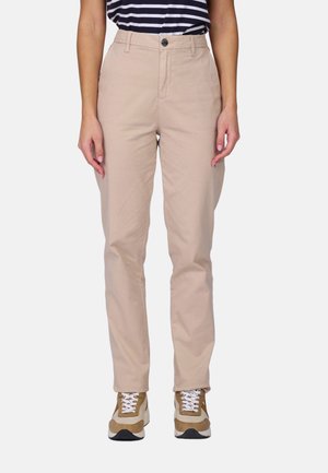 Femme portant un pantalon beige droit, des baskets marron et blanches, et un haut rayé bleu marine et blanc, debout les bras détendus.