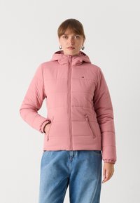 Roze gevoerde jas met een capuchon, voorzien van een rits aan de voorkant, verticale stiksels en zijzakken. Draag het over blauwe spijkerbroeken.