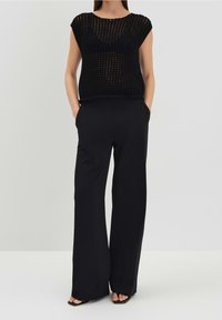 Mustat neulotut paidat, joissa on lyhyet hihat ja löysä istuvuus, yhdistettyinä leveälahkeisiin mustiin housuihin. Sileä tekstuuri, minimaalinen muotoilu ja rento tyyli.