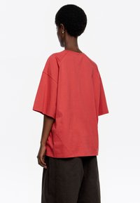 Camiseta roja de gran tamaño con mangas cortas y escote redondo, que presenta un corte relajado y una textura de tela suave. La parte trasera tiene un detalle de costura.