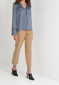 Camisetta a maniche lunghe, a righe blu e bianche, con colletto e taschino sul petto, abbinata a pantaloni beige a gamba affusolata e sabot neri con tacco blocco.