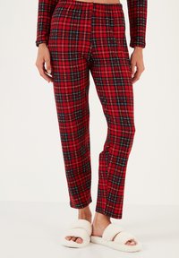 Pantalones de pijama a cuadros rojos y negros con cintura elástica, piernas ajustadas y una textura suave, combinados con zapatillas blancas y esponjosas.