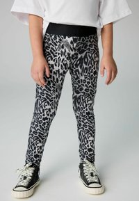 Leggingi s uzorkom životinjskog printa u crnoj i sivoj boji s čvrstim crnim pojasom, upareni s visokim tenisicama koje imaju vezice s logotipom.
