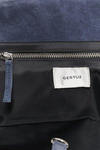 Laivastonsininen mokkanahkainen käsilaukku, jossa musta kangasvuori, hopeanvärinen vetoketju ja valkoinen etiketti, jossa lukee "GESTUZ". Mukana on myös sopiva vetoketjun vetonappi.