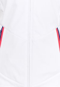 White jacket with blue and red side stripes, featuring smooth fabric, a central zipper, and tailored seams for a fitted design.