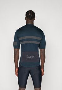 Maillot de cyclisme à manches courtes en bleu marine avec des rayures grises. Il présente une poche zippée à l'arrière avec le logo "Rapha" et une coupe athlétique élégante.