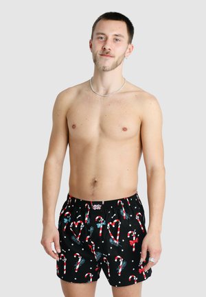 Black boxer shorts featuring a playful pattern of candy canes, bows, and stars in red, white, and blue. Elastic waistband for comfort.