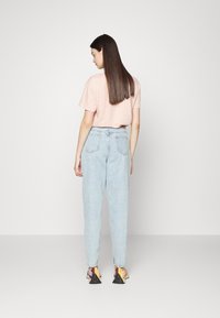 T-shirt de manga curta rosa claro, jeans de cintura alta azul claro e ténis multicoloridos. Tecido suave com um corte descontraído.