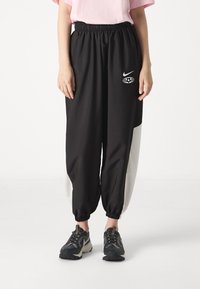 Svarta joggerbyxor med en vit accent, elastisk midjeband och rynkade muddar. Har en Nike-logotyp och en grafisk design på låret.