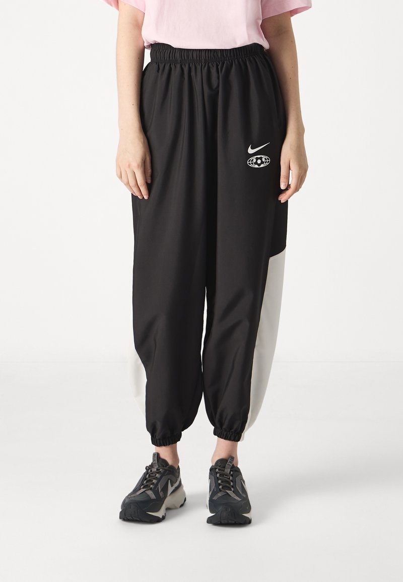 Svarta joggerbyxor med en vit accent, elastisk midjeband och rynkade muddar. Har en Nike-logotyp och en grafisk design på låret.