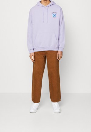 Ljuslila hoodie med framficka och grafisk detalj, kombinerad med bruna vida byxor och vita sneakers.