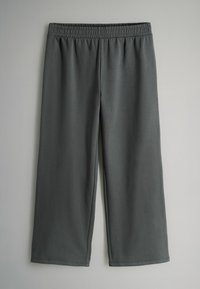 Pantalons larges gris foncé avec ceinture élastique, étalés à plat sur un fond gris clair.