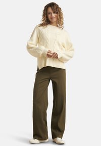 Cream cable-knit sweater with a relaxed fit, featuring ribbed texture. Paired with loose olive green pants and white sneakers.