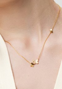 Złoty naszyjnik z małymi wisiorkami w kształcie motyla i serca, z teksturowanym łańcuchem oraz błyszczącym akcentem na jednym z motyli.