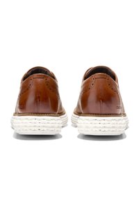 Scarpe in pelle marrone con dettagli brogue, suola in gomma bianca testurizzata e retro arrotondato. Superficie liscia con cuciture a contrasto.